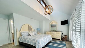 Un dormitorio con cama, tocador, televisor y ventana con persianas.