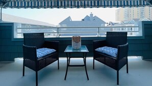 Un espacio cubierto al aire libre con dos sillas de mimbre y una mesa, con vista a un barrio residencial.