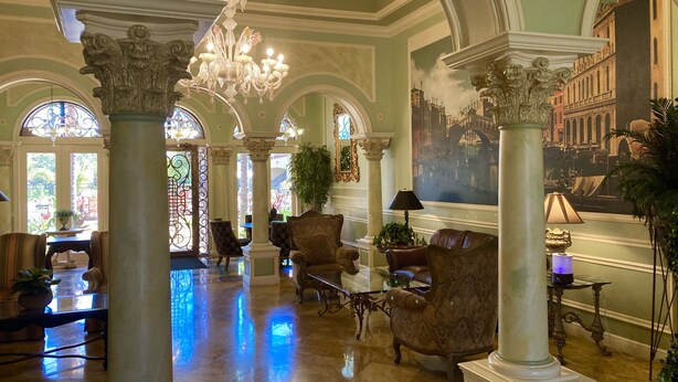 Un lobby imponente con techos altos, columnas decorativas y un candelabro.