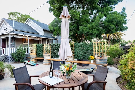 An outdoor patio with wooden tables and chairs, a large umbrella, and a decorative fence.