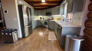 A modern kitchen with wooden floors, stainless steel appliances, and light gray cabinets. - Secluded Lake View Log Cabin on 40 Acres (Yankton)