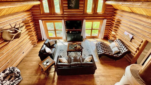 A log cabin interior with a fireplace, leather sofas, and a television. - Secluded Lake View Log Cabin on 40 Acres (Yankton)