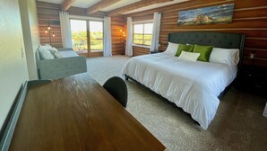 A bedroom with a bed, a desk, and a chair. There is a window with curtains and a view of greenery outside. - Secluded Lake View Log Cabin on 40 Acres (Yankton)