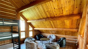 A cozy attic room with a wooden sloped ceiling, a bunk bed, a round table, and two bean bags. - Secluded Lake View Log Cabin on 40 Acres (Yankton)
