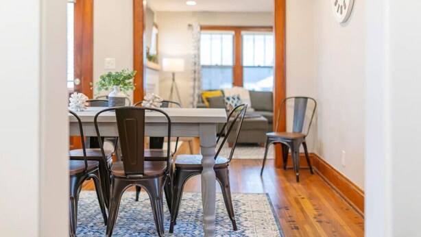 Un comedor con una mesa y sillas de madera, una araña y vistas a una sala de estar con un sofá y una lámpara.