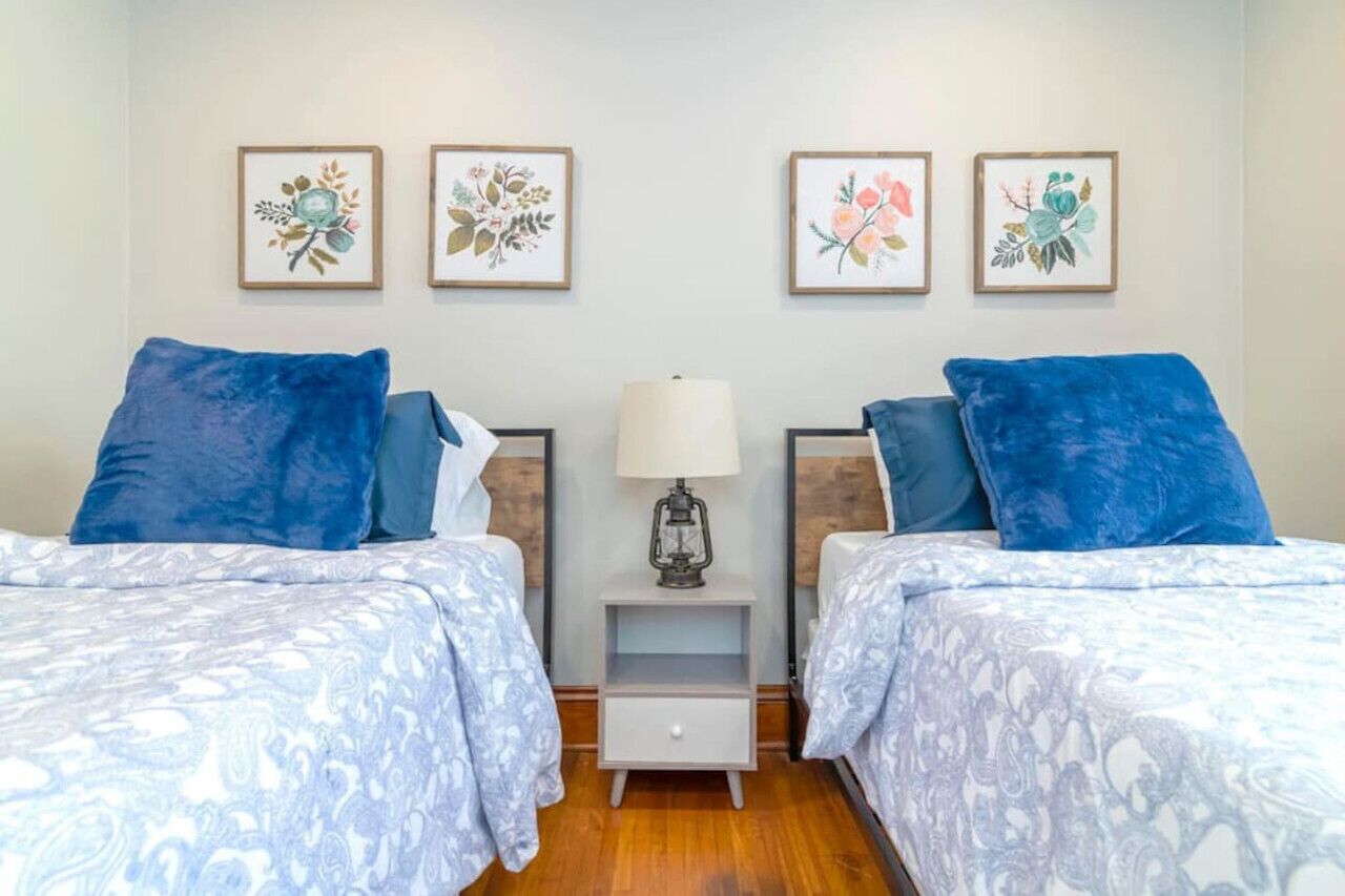 Une chambre avec deux lits, une table de chevet et quatre œuvres d’art florales encadrées accrochées au mur.