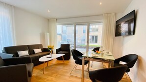 Una sala de estar moderna con un sofá, sillas, una mesa de centro y una mesa de comedor con un florero.