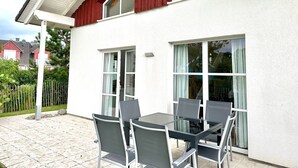 A patio with a table and chairs, large windows, and a red exterior wall.