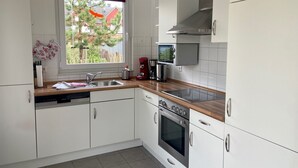 A modern kitchen with white cabinets, a wooden countertop, a built-in oven, a microwave, and a window with a view of trees and a red building.