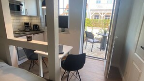 Ein kompaktes Studioapartment mit Küchenzeile, Essbereich und kleinem Balkon.