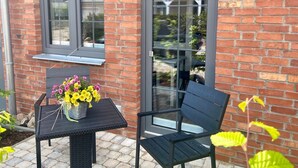 Eine Terrasse mit Tisch und Stühlen, einer Blumenkomposition und einer Ziegelwand mit Fenstern.