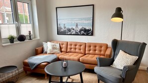 Una sala de estar con un sofá de cuero marrón, un sillón gris, una mesa redonda de centro y un cuadro en la pared.