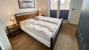 Un dormitorio con una cama de madera, una mesita de noche con lámpara, un cuadro enmarcado en la pared y una ventana con persianas.