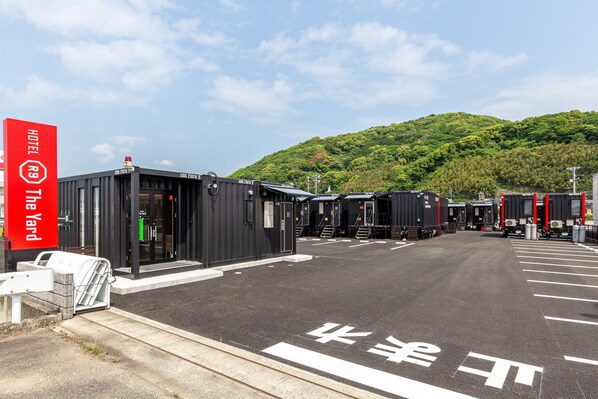 A hotel with a modern design, featuring a prominent red sign, a parking area, and a mountainous backdrop. - HOTEL R9 The Yard Kohoku (Kohoku)