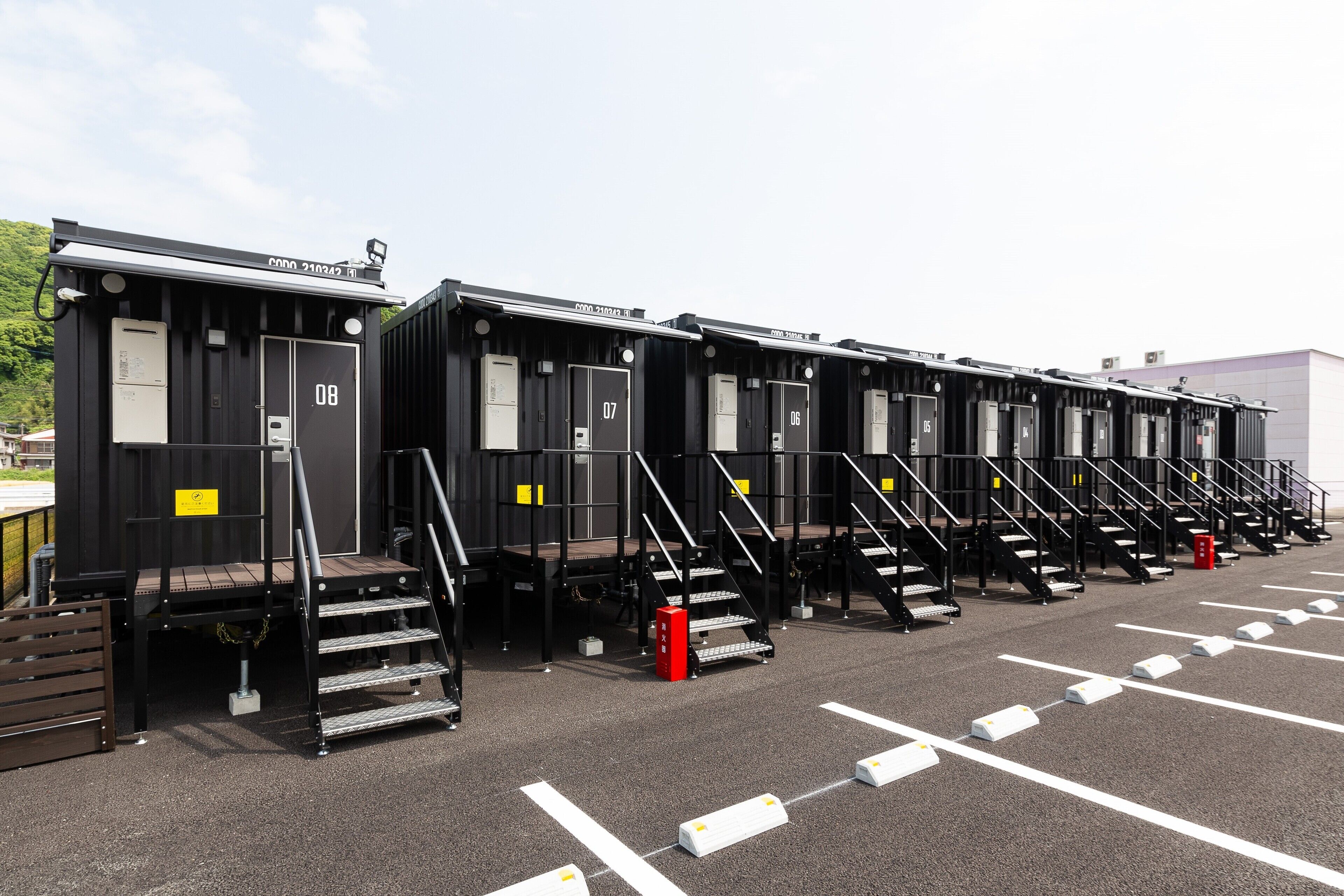 A row of black portable cabins with numbered doors, each with a small staircase leading to the entrance.