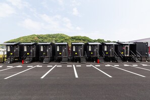 A row of portable restrooms with numbered doors, steps leading up to each, and a parking lot in front. - HOTEL R9 The Yard Kohoku (Kohoku)