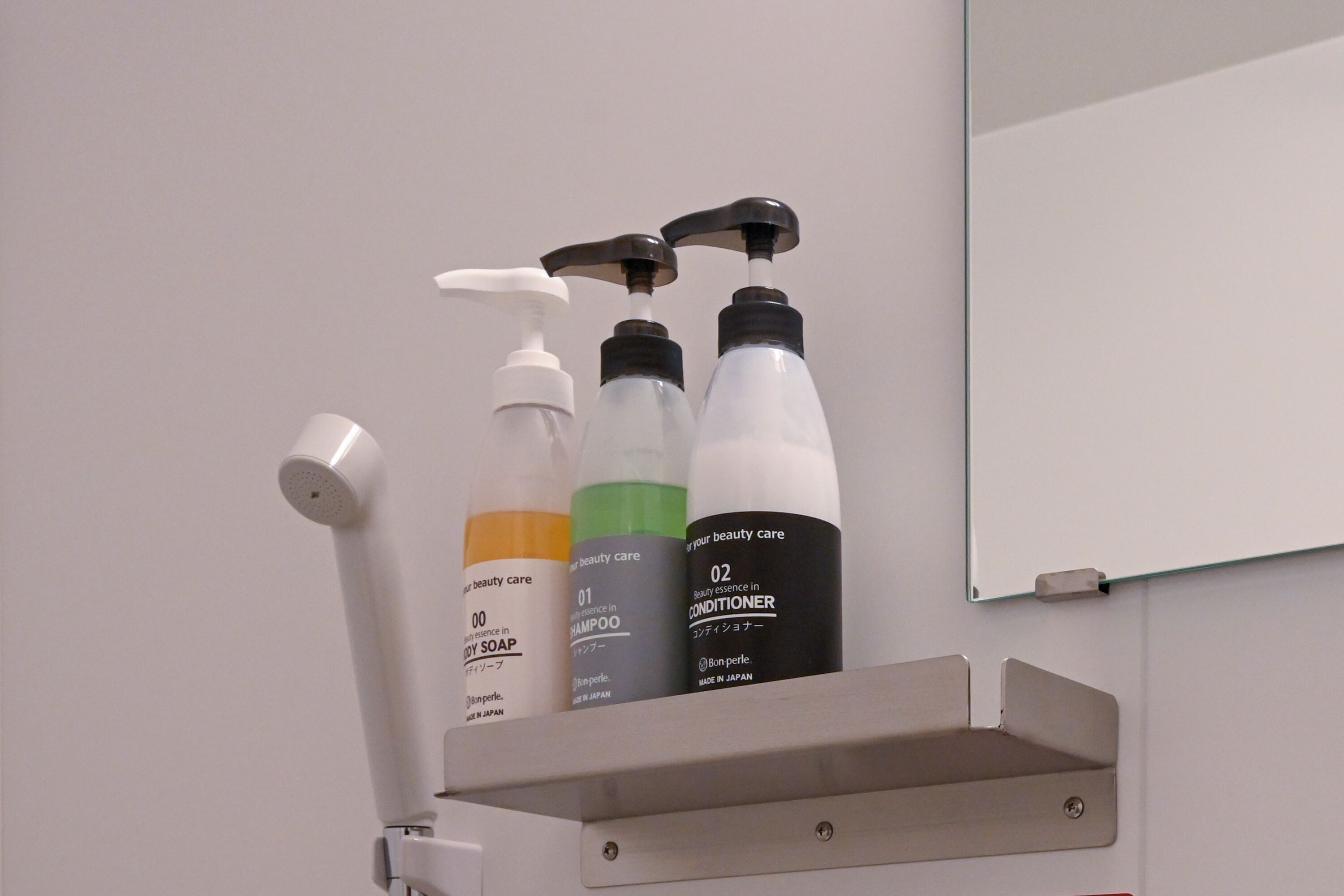 Un estante de baño con tres botellas de productos de tocador y un cabezal de ducha manual blanco.