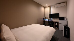 Una habitación de hotel con cama, escritorio con computadora, televisor y aire acondicionado.
