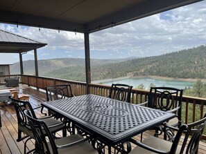 Eine überdachte Terrasse mit Tisch und Stühlen mit Blick auf einen See und bewaldete Hügel.