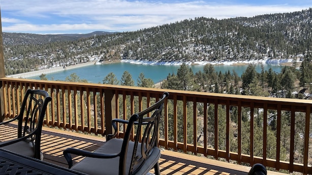 Un balcon offrant une vue sur un lac, bordé d’arbres couverts de neige et sur une colline boisée.