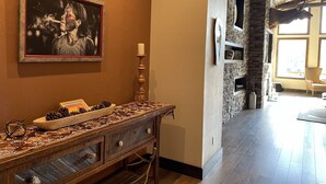 Une console en bois ornée d’une bougie, d’un tableau encadré et d’objets décoratifs. On aperçoit également une cheminée en pierre et un fauteuil à l’arrière-plan.