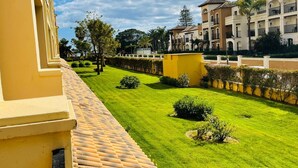 A courtyard with a well-maintained lawn, a yellow wall, and a tiled roof. - Charming beach apartment. Urb Canela Park (Playa de Isla Canela)