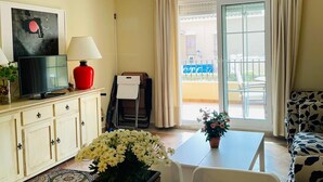 A room with a television, a lamp, a table with a potted plant, a patterned rug, and a sofa. - Charming beach apartment. Urb Canela Park (Playa de Isla Canela)