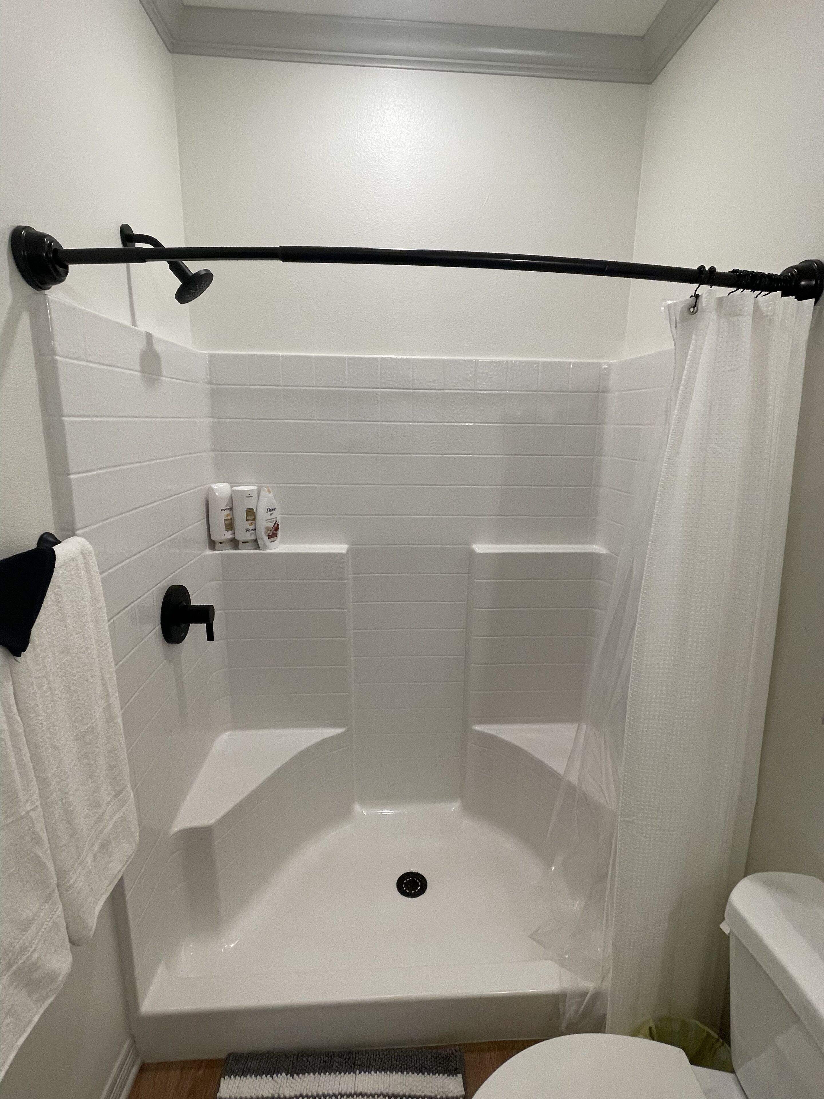 Een douchegedeelte met een betegelde muur, een zwarte douchegordijnrail en een toilet.