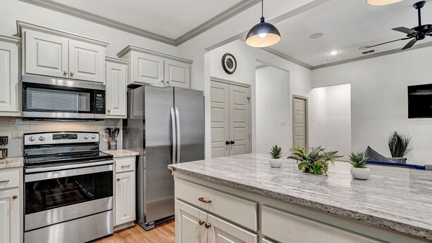 A modern kitchen with white cabinetry, stainless steel appliances, and a marble countertop.