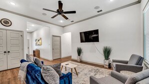 A modern living room with a blue sofa, grey armchairs, a small table, and a ceiling fan.