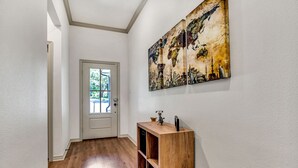 A hallway with a wooden floor, a white door, and a wall-mounted artwork depicting a cityscape.