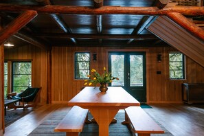 A wooden interior with a large table, benches, and a vase of yellow flowers.