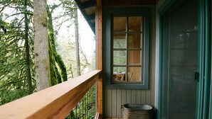 A wooden deck with a metal railing, a window with a view of trees, and a metal pot on the floor.