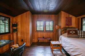 A wooden cabin room with a bed, a desk, and a chair.