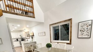 Ein Essbereich mit einem Holztisch und Stühlen, einer Bank, einer Topfpflanze und einem gerahmten Bild an der Wand.