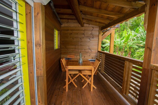 Ein Holzinterieur mit Tisch und Stühlen, einem Fenster mit Jalousien und Blick ins Grüne.