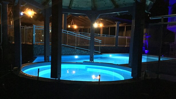 Una piscina interna con una parete in pietra e un soffitto in legno.