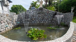 Una fontana in pietra con getti d'acqua, circondata da un bordo in pietra a cerchio e uno stagno ricoperto di ninfee.