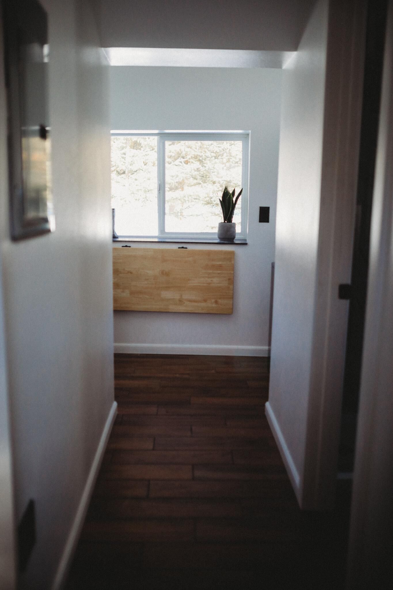 Un pasillo estrecho con un banco de madera, una ventana con vistas a árboles y una planta en maceta en el alféizar.