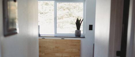 Un pasillo estrecho con un banco de madera, una ventana con vistas a árboles y una planta en maceta en el alféizar.