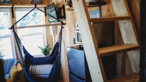 Ein Hängestuhl in einem Zimmer mit Holzwänden, einem Schreibtisch mit Computer und einem Fenster mit Blick auf Bäume.