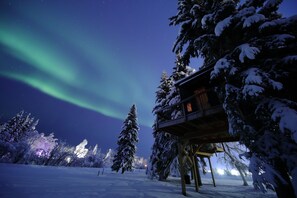 A snow-covered landscape with a wooden viewing platform and a building with illuminated windows. - This memorable stay is anything but ordinary (Fairbanks)