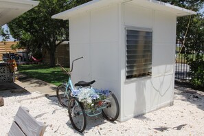 Un petit abri de jardin blanc, avec une fenêtre, et un vélo garé devant.