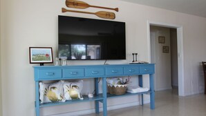 Ein blauer Konsolentisch mit einem Flachbildfernseher darüber, einem gerahmten Bild und dekorativen Accessoires.