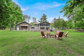 Et toetagers hus med stenvægge, pejse og røde Adirondack-stole i haven.