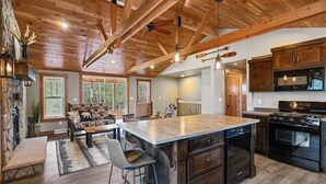 A spacious kitchen with a large island, wooden beams on the ceiling, and a stone fireplace.