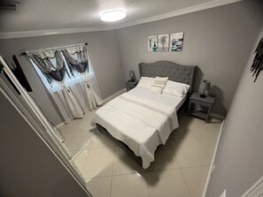 A bedroom with a bed, nightstands, a window with curtains, and wall art. - House (Tampa)