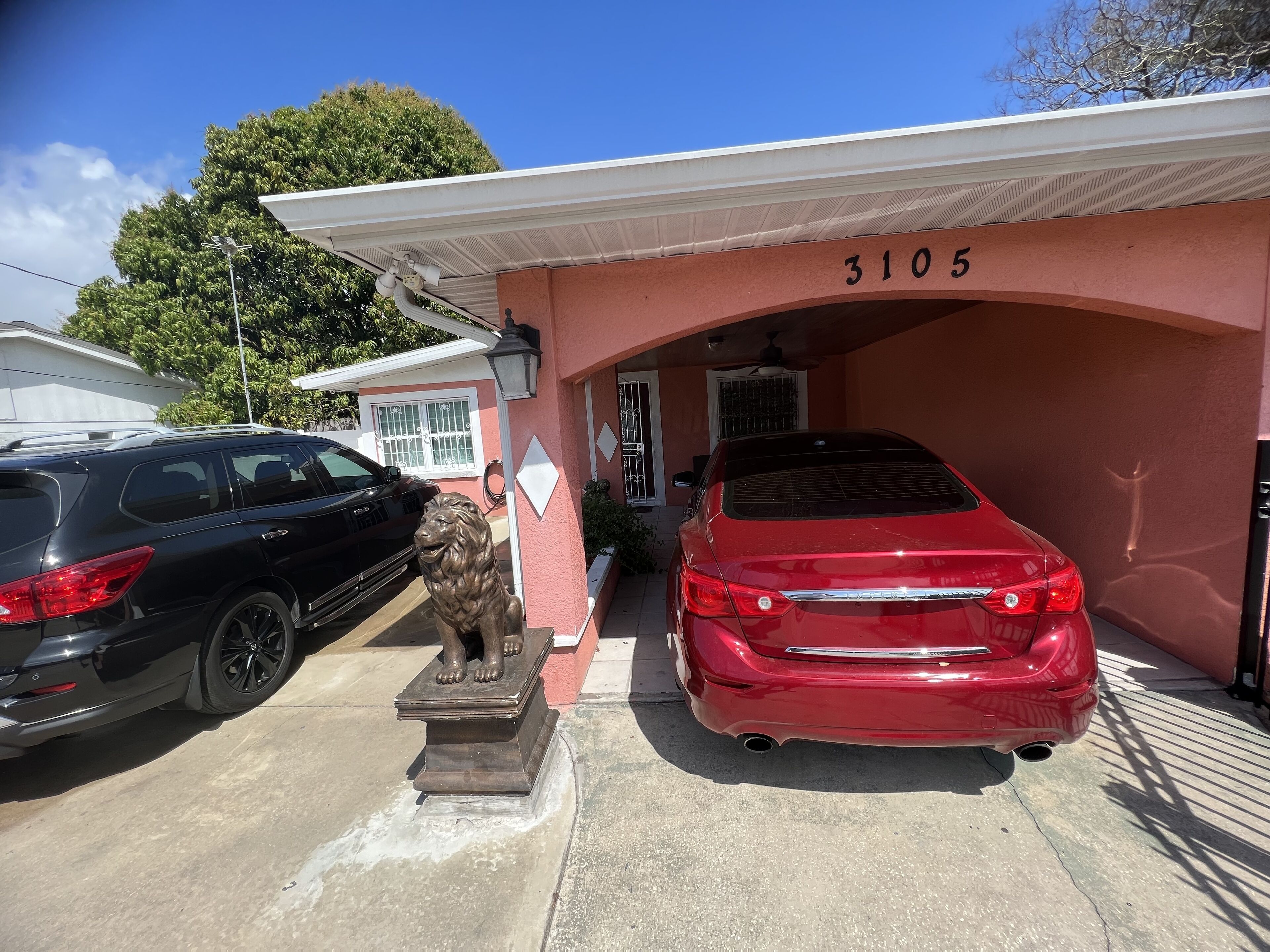 A building with the number 3105, two parked cars, a lion statue, and a covered entrance.
