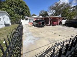 A residential driveway with two parked cars, a gated entrance, and a house with a red roof. - House (Tampa)