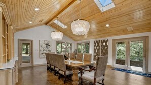 Un'ampia sala da pranzo con un tavolo e sedie in legno, ampie finestre e un soffitto alto con travi in legno.